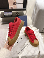 Pair of red lace-up low-top sneakers with tan soles, held up for display
