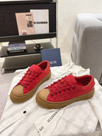 Red lace-up low-top sneakers with tan sole, side view of the pair