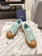 Two light blue lace-up sneakers with tan gum soles on white fabric