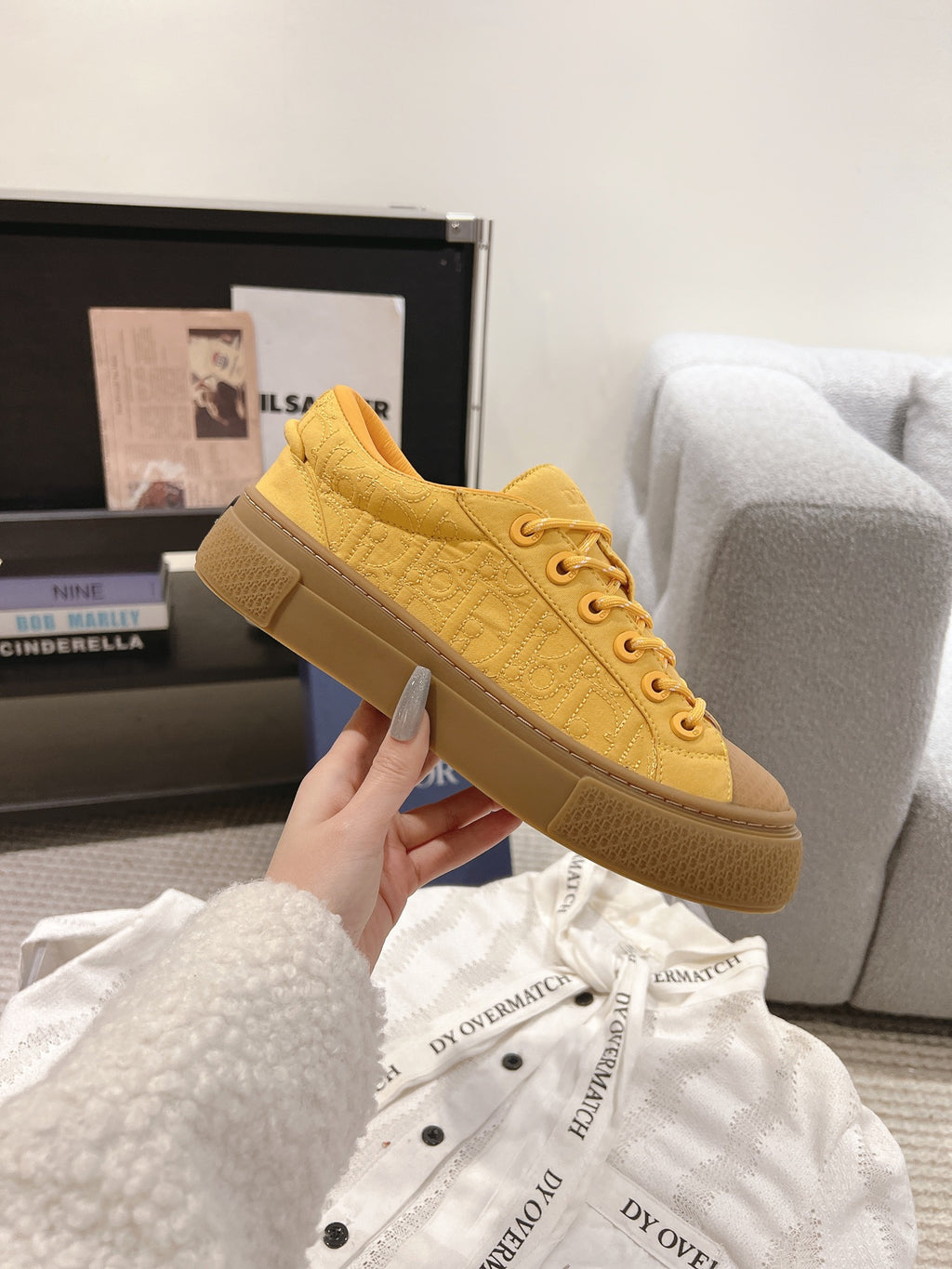 Yellow low-top unisex sneaker held in hand, lace-up front and rubber sole