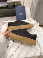 Two black Dior lace-up sneakers with tan soles laid on fabric