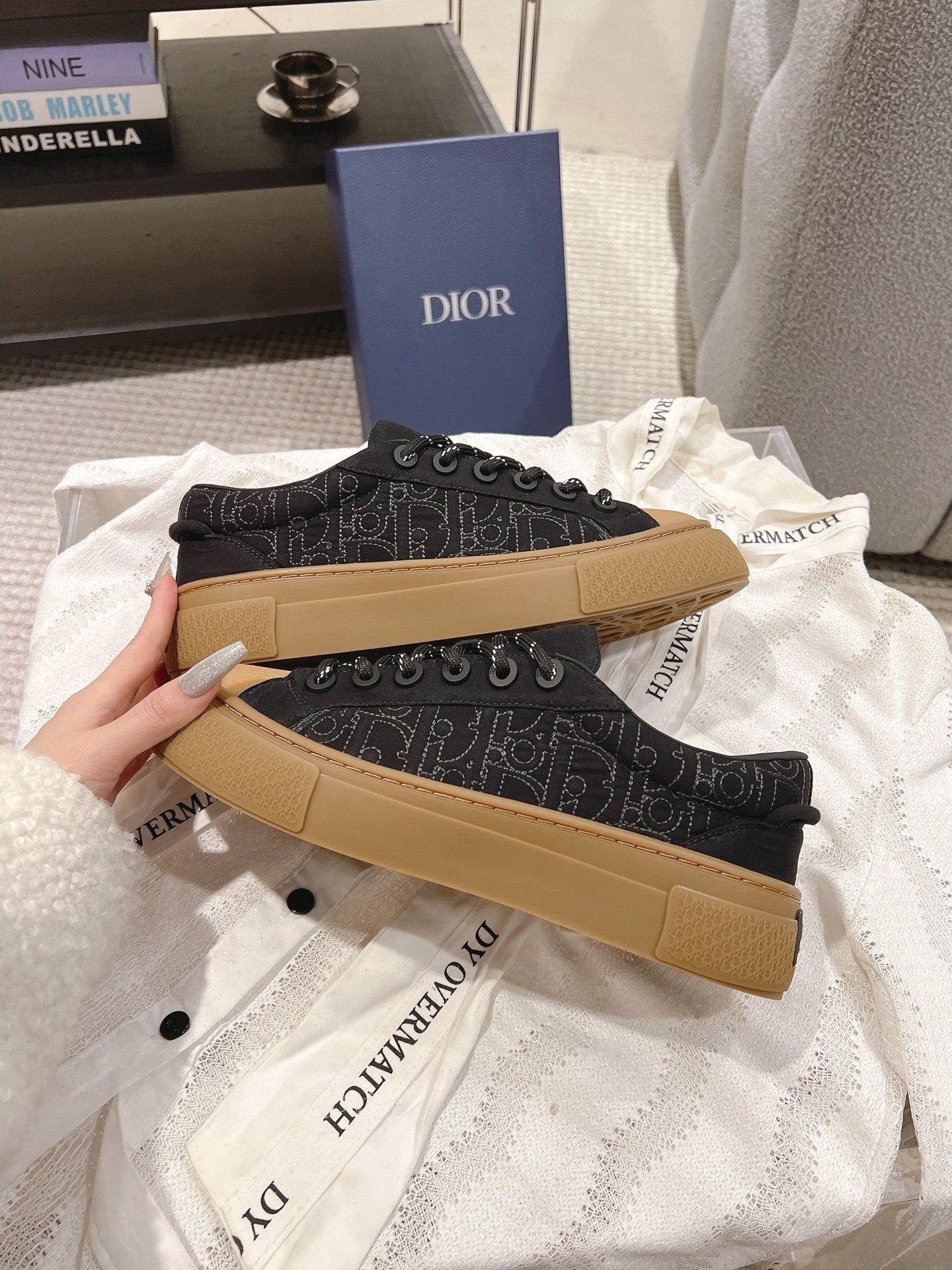 Two black Dior lace-up sneakers with tan soles laid on fabric