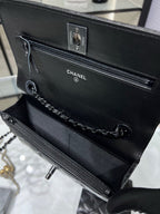 Black leather flap bag showing top handle loop, front zipper, and CC branding
