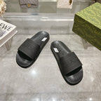 Pair of black Gucci slide sandals with embossed GUCCI logo strap