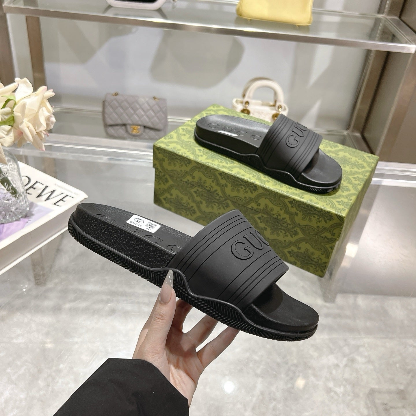 Hand holding black Gucci slide sandal showing ridged outsole and GUCCI logo
