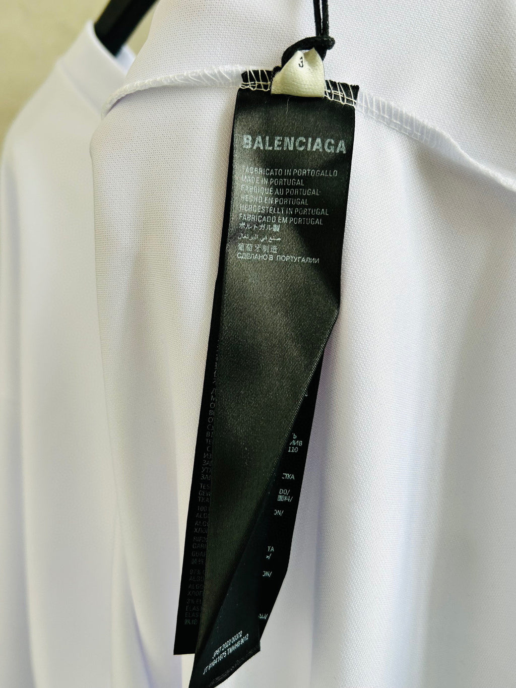 Brand label tag inside neckline on white long-sleeve top with black text