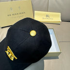 Burberry cap in black with gold button on top and partial gold TB emblem.