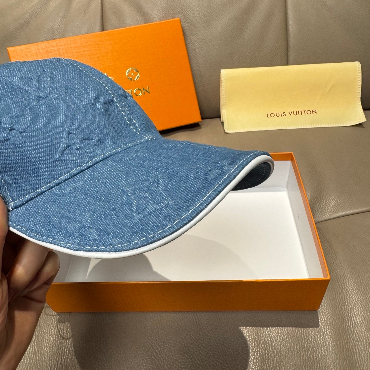 Blue denim cap brim detail with visible stitching and embossed monogram