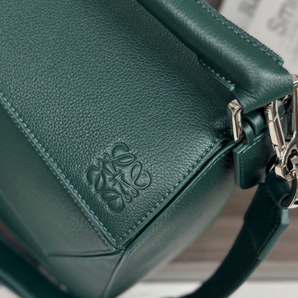 Teal leather bag corner with embossed logo, stitched seam detail, and metal ring hardware.