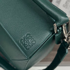 Teal leather bag corner with embossed logo, stitched seam detail, and metal ring hardware.