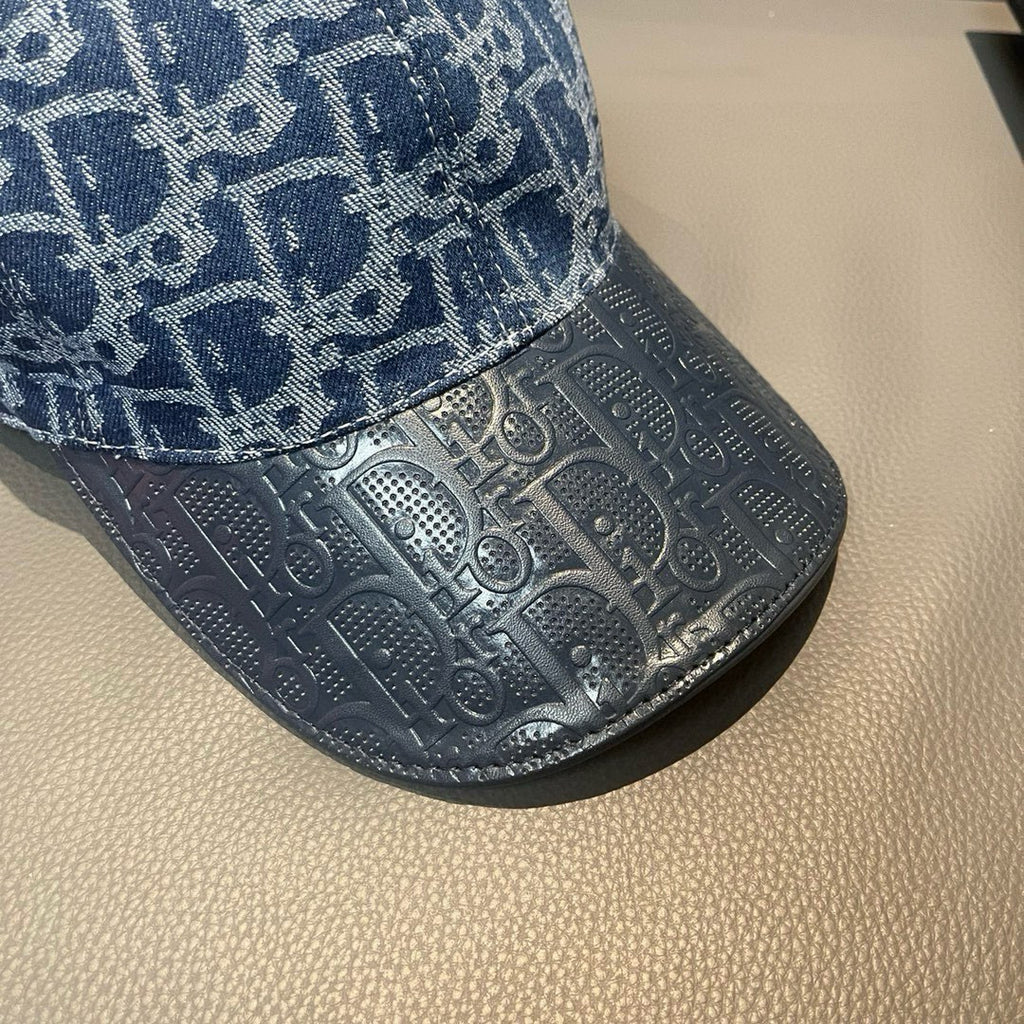 Close-up of blue cap brim with embossed monogram pattern texture and stitched edge.