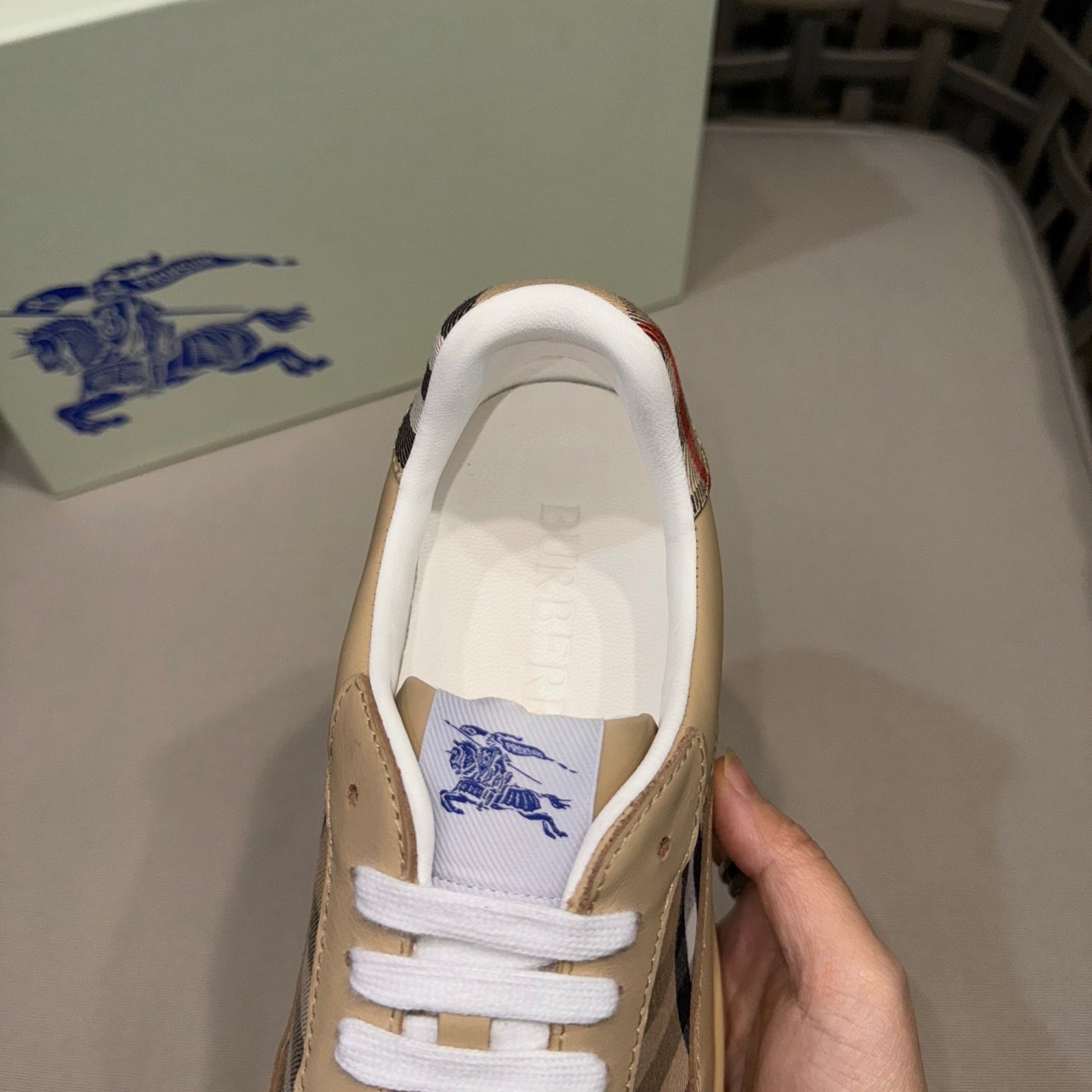 Beige low-top sneaker with white laces and blue logo on tongue