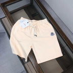 Cream drawstring shorts with elastic waistband and circular logo patch on leg