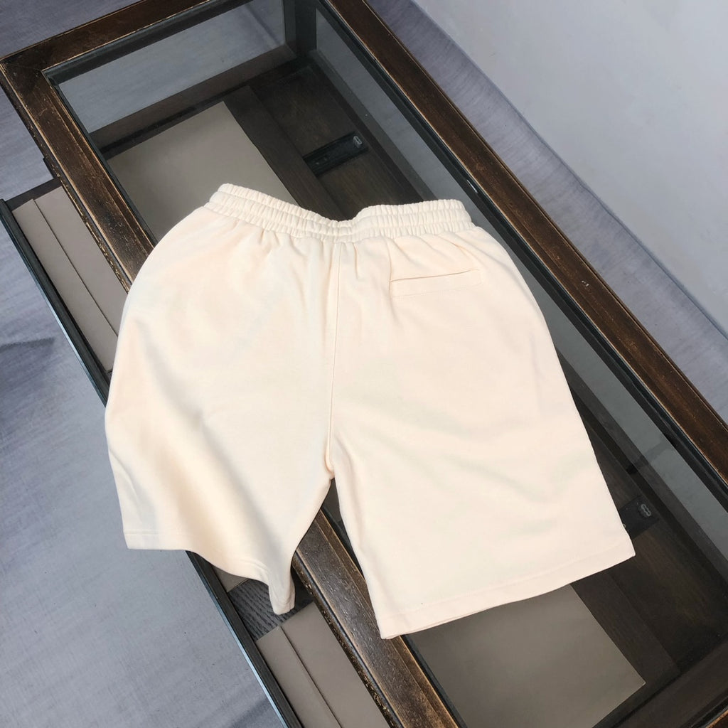 Cream shorts with elastic waistband and drawstring, side logo patch visible