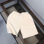Cream shorts with elastic waistband and drawstring, side logo patch visible