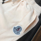 Cream shorts with elastic waistband, drawstring, and circular logo patch detail