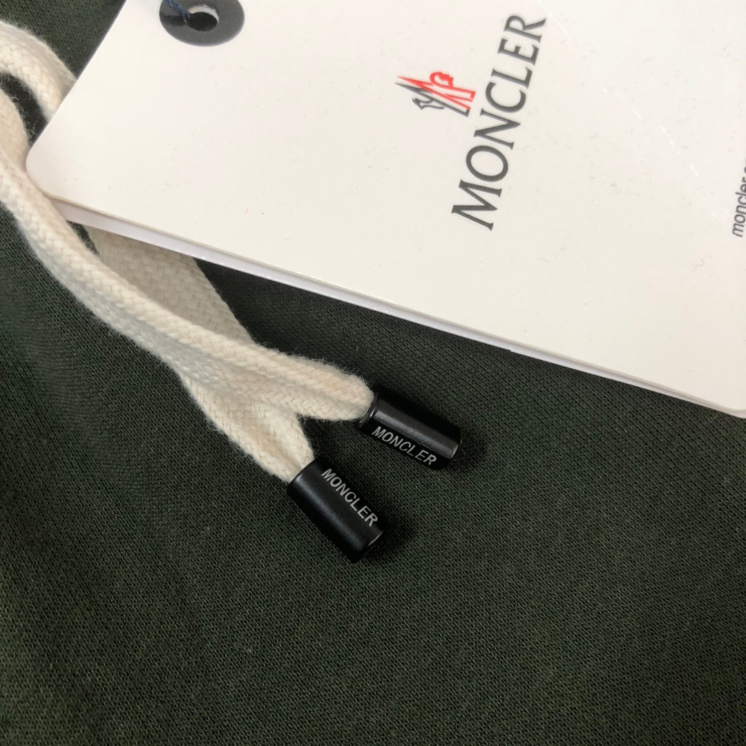 Dark green drawstring shorts with white MONCLER tag and small black logo patch