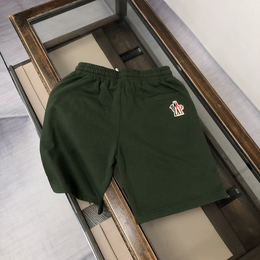 Dark green drawstring shorts with small red-and-white logo on right thigh