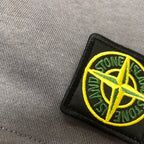 Close-up of embroidered Stone Island logo patch on gray shorts
