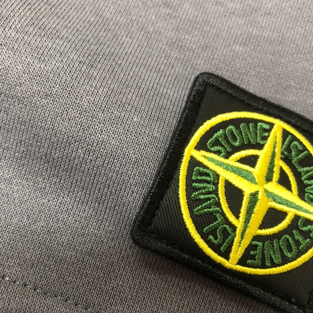 Close-up of embroidered Stone Island logo patch on gray shorts
