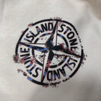 Close-up of circular Stone Island logo graphic on cream shorts fabric