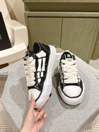 Black and white low-top sneakers held by hand, side view with white panel stripes.