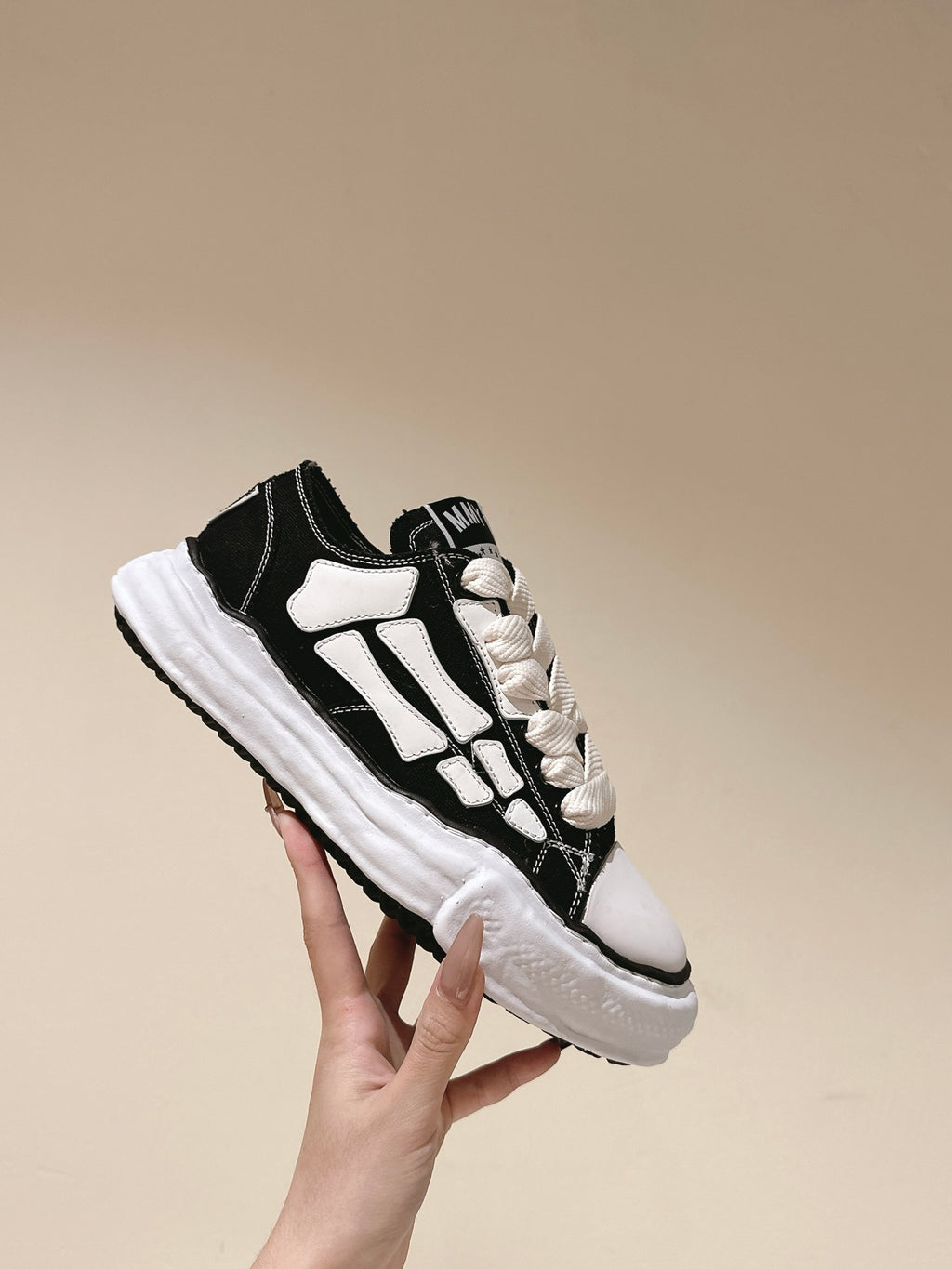 Black and white low-top sneaker held up, side profile with white graphic stripes.