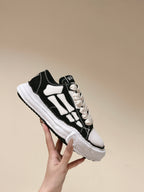 Black and white low-top sneaker held up, side profile with white graphic stripes.