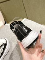 Black low-top sneaker with white outsole, heel and logo tab close-up in hand.