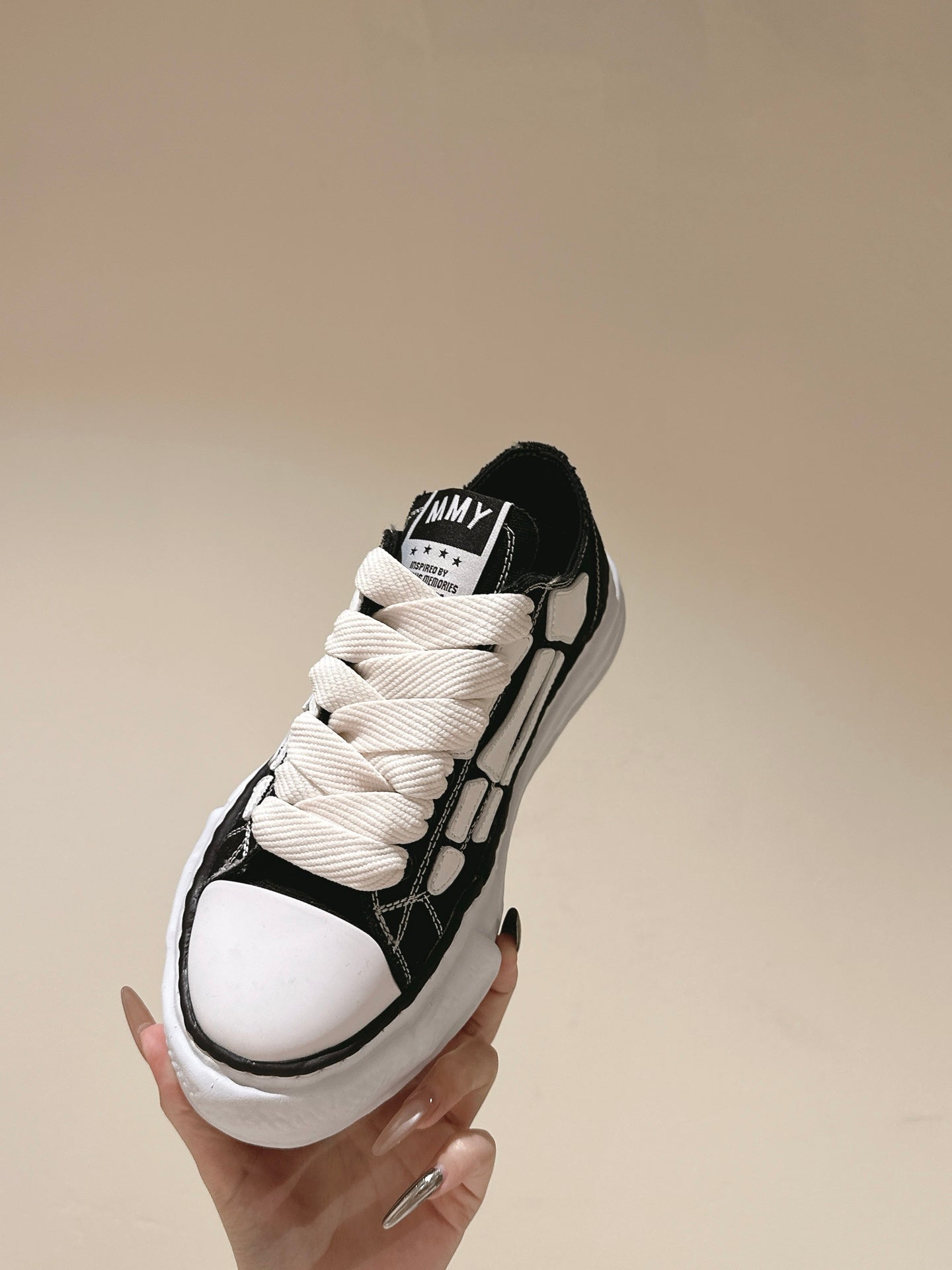 Black and white low-top sneaker held up, front view with white laces and toe cap.