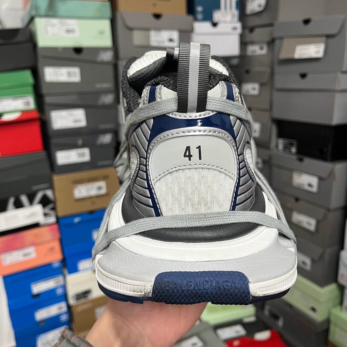 Heel and back view of grey athletic shoes with blue sole edge and numbered patch.