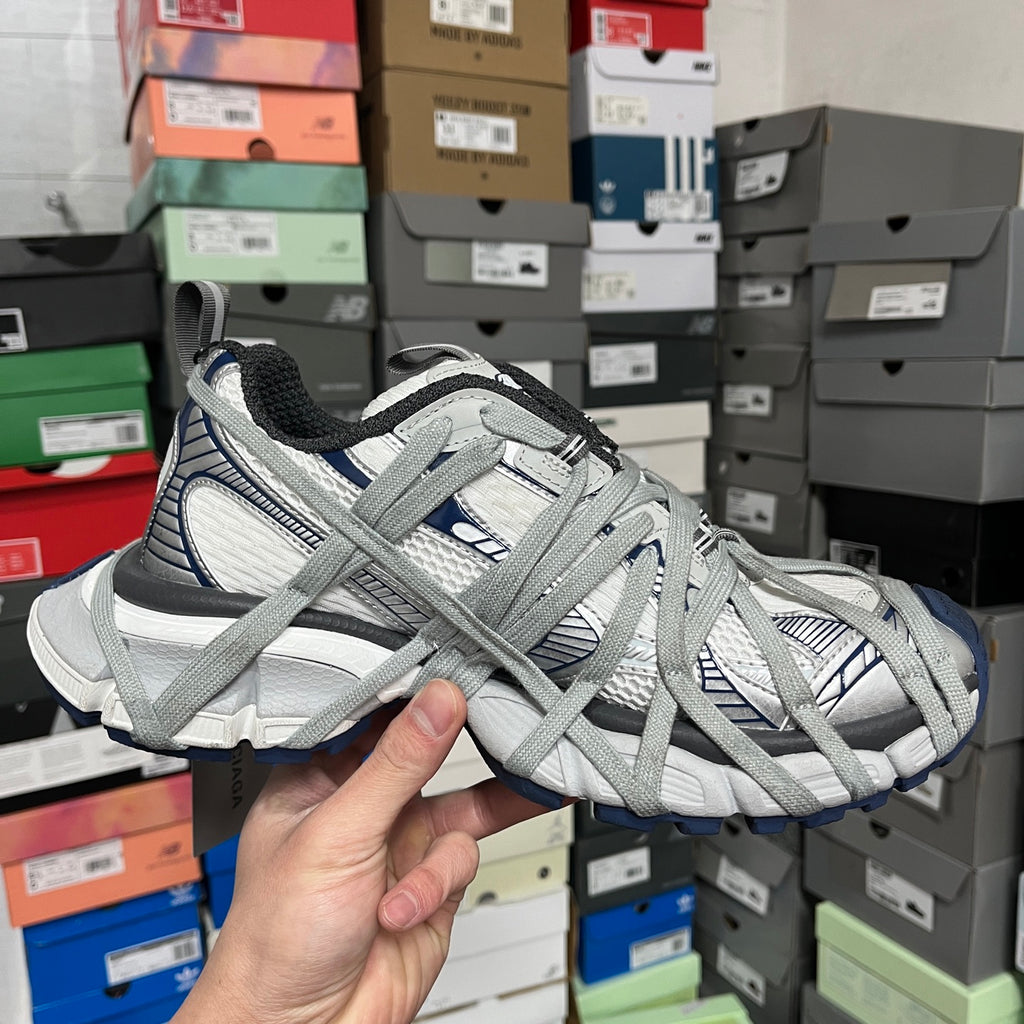 Pair of grey and white lace-up athletic shoes with blue accents held in hand.