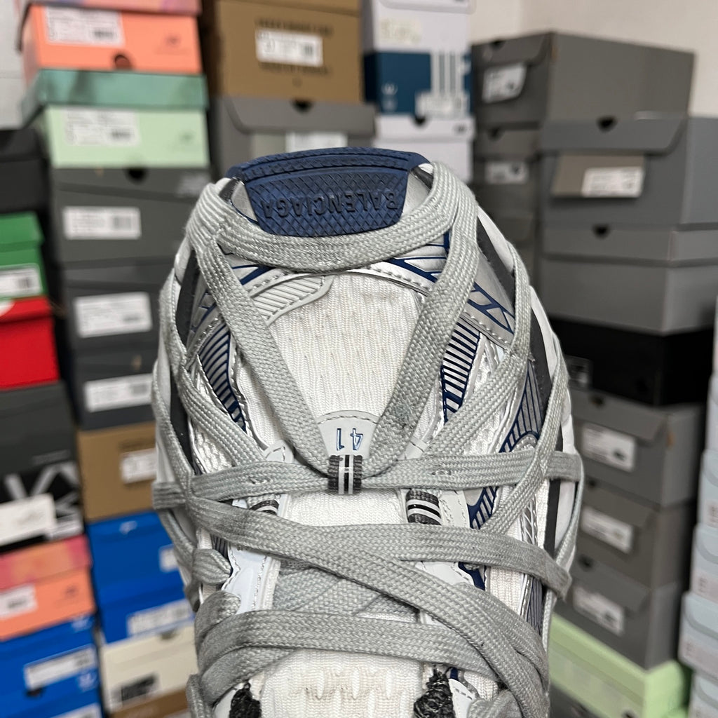 Front view of grey athletic shoes with blue heel patch, mesh panels, and laces.
