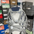 Front view of grey athletic shoes with blue heel patch, mesh panels, and laces.