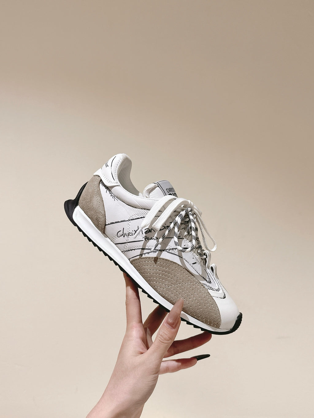 Dior unisex sneaker, white and beige lace-up with black sole, held by hand