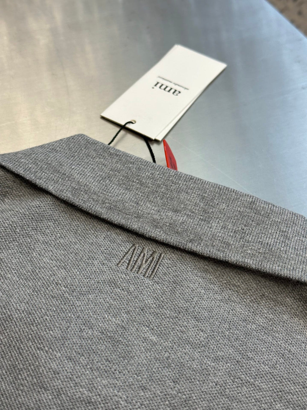 Light gray polo shirt hem with embroidered AMI logo