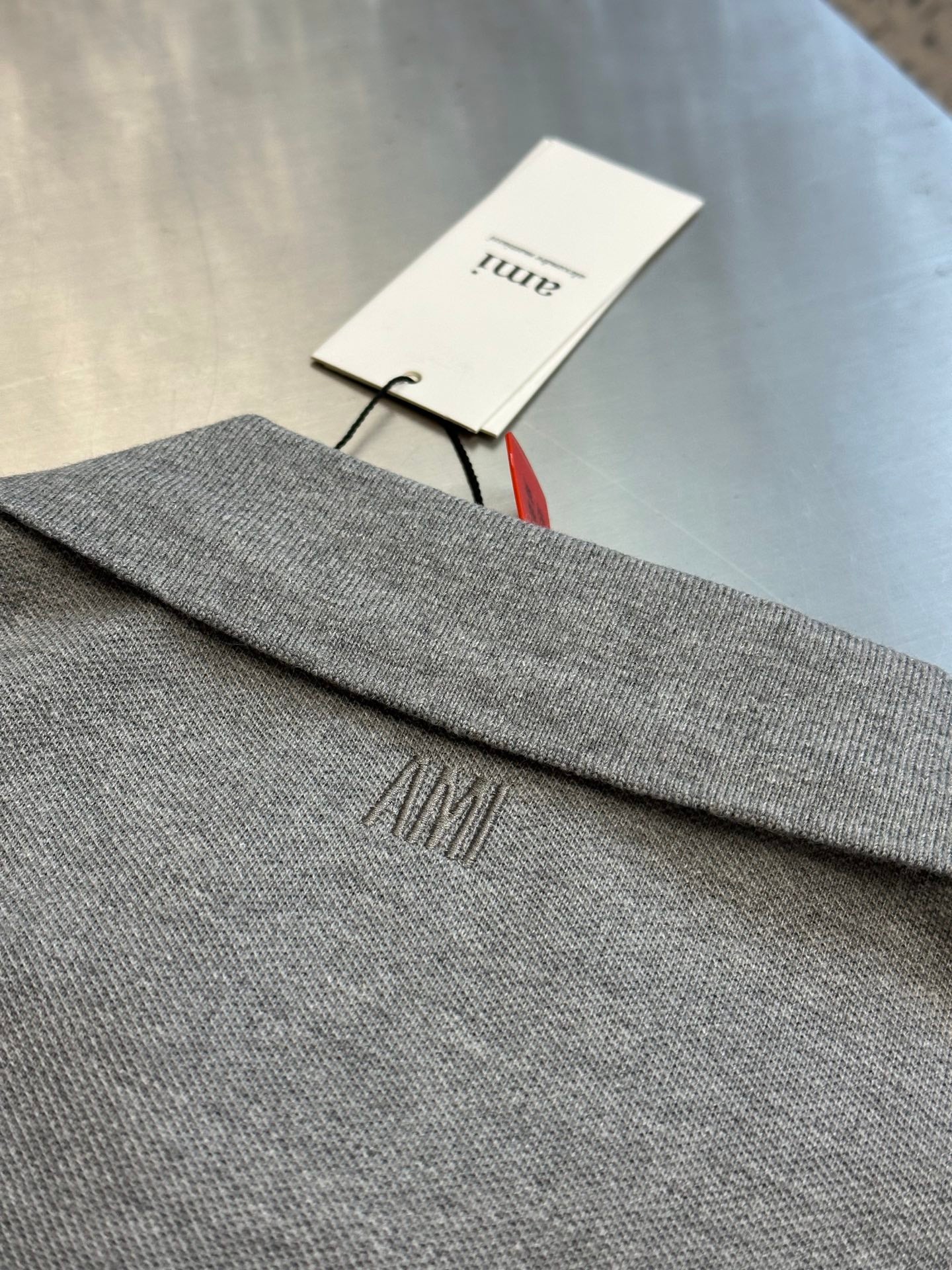 Light gray polo shirt hem with embroidered AMI logo