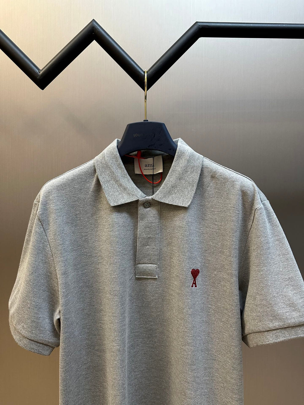 Gray polo shirt front view with pointed collar, button placket, and red heart A detail