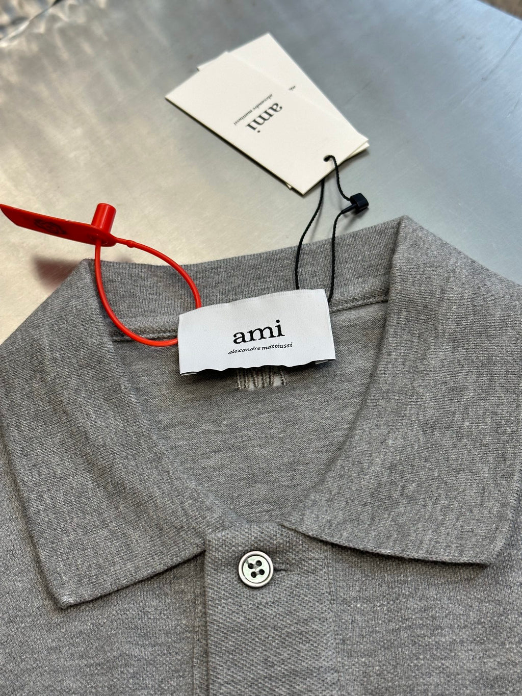 Gray polo shirt neckline with pointed collar, button closure, and attached clothing tags