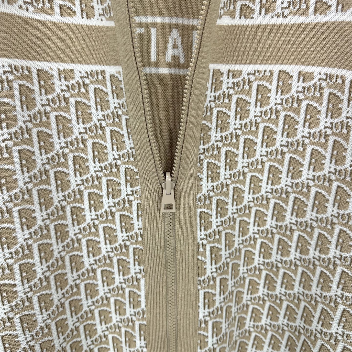 Beige knit jacket close-up of center zipper and white monogram pattern