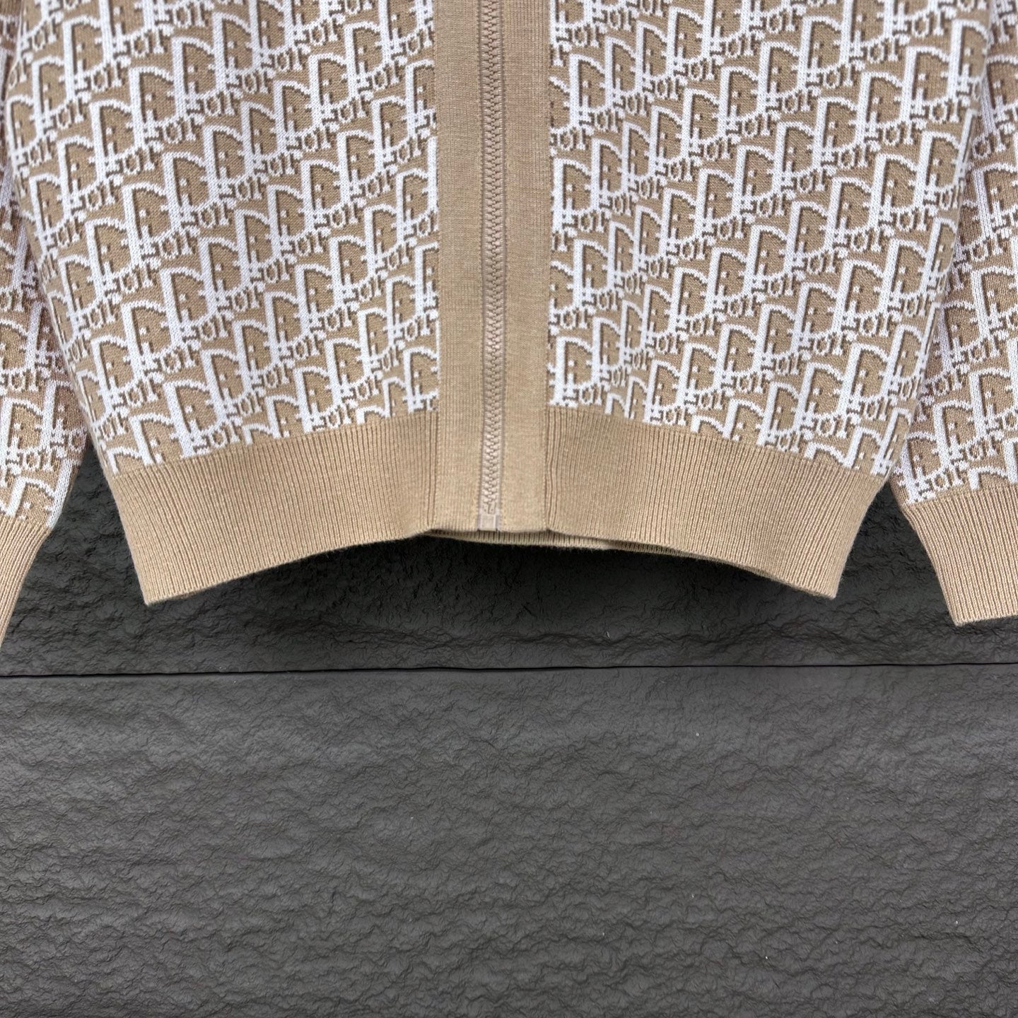 Beige knit zip jacket hem close-up with white monogram panels and ribbed cuff