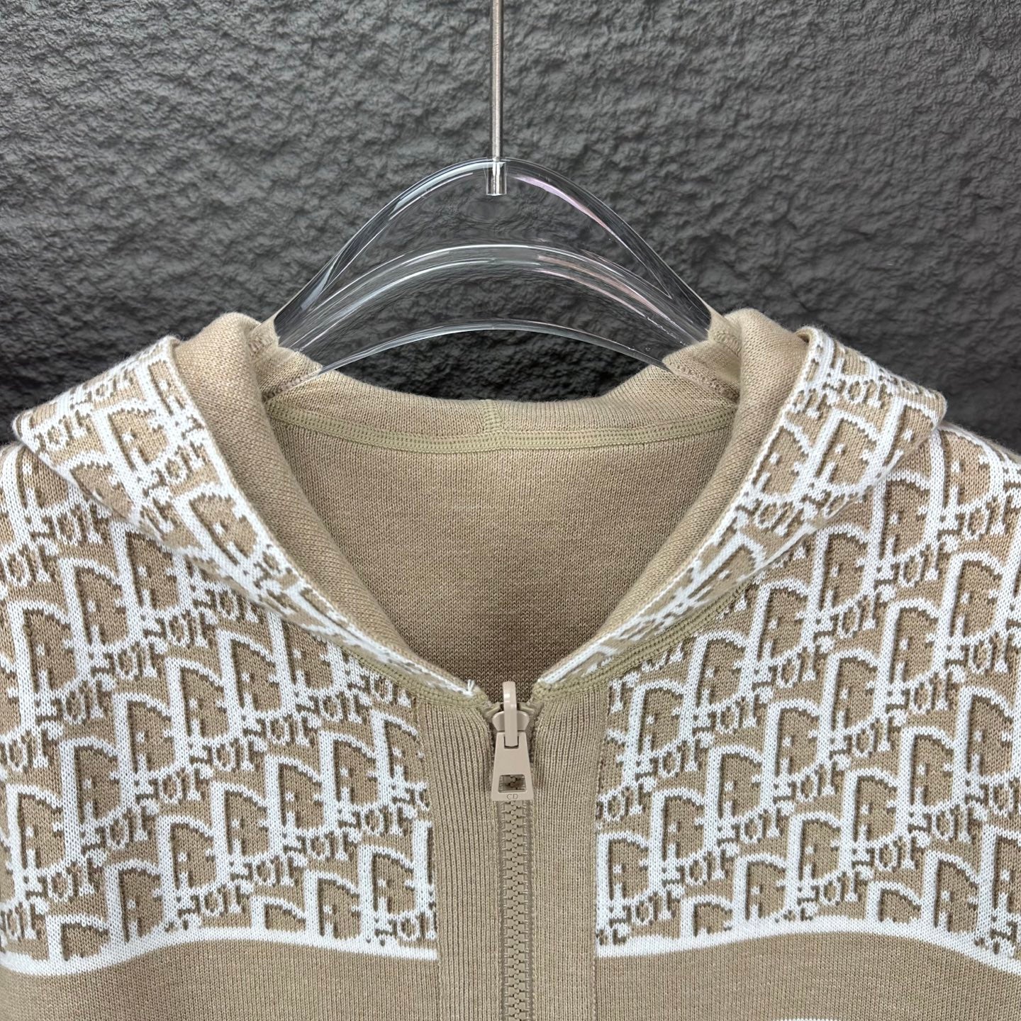 Beige hooded zip jacket close-up with white monogram knit and zipper pull