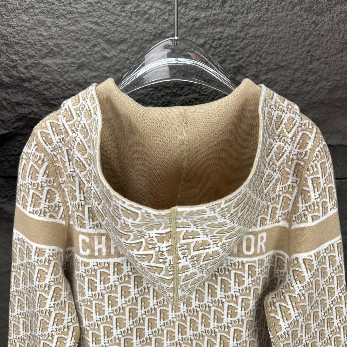 Beige knit hooded zip jacket close-up with white monogram pattern at neckline