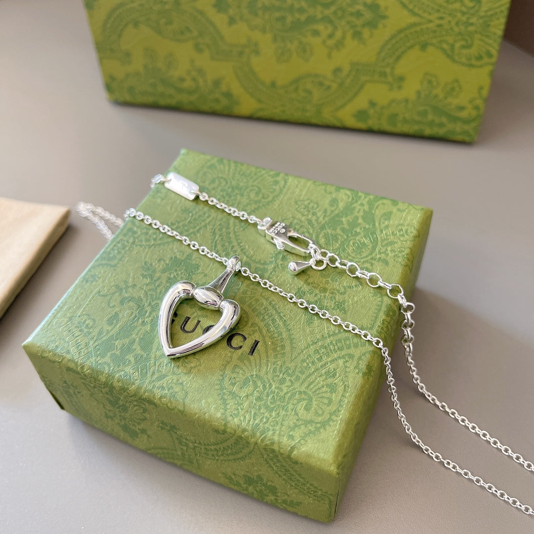 Silver charm necklace with heart pendant and tag accents displayed on green box