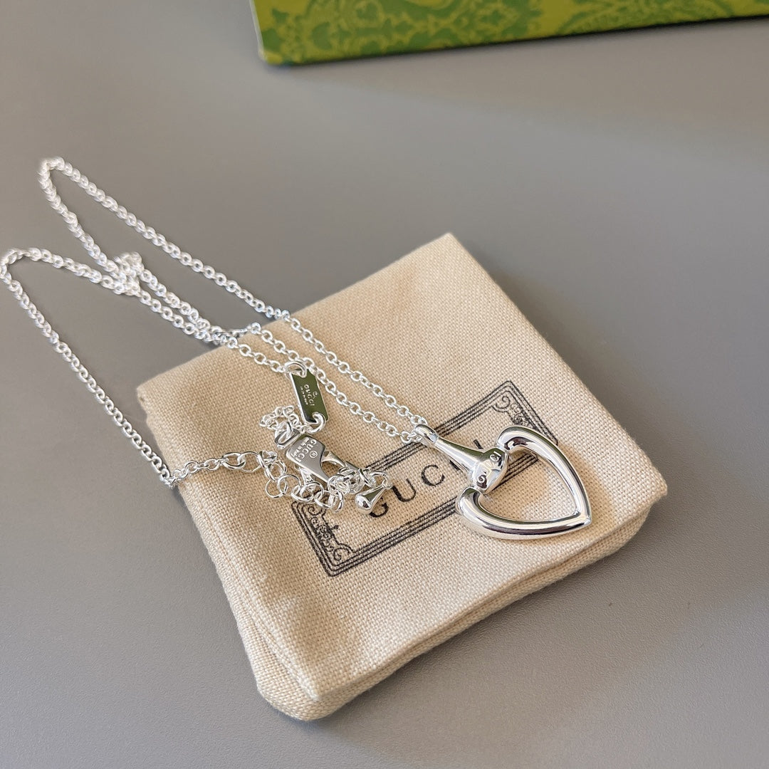 Silver heart pendant necklace with small charm pieces on beige fabric pouch