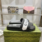 Black slide sandals with white Gucci logo strap on textured footbed