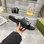 Black Gucci slide sandal with striped outsole and white Gucci logo strap