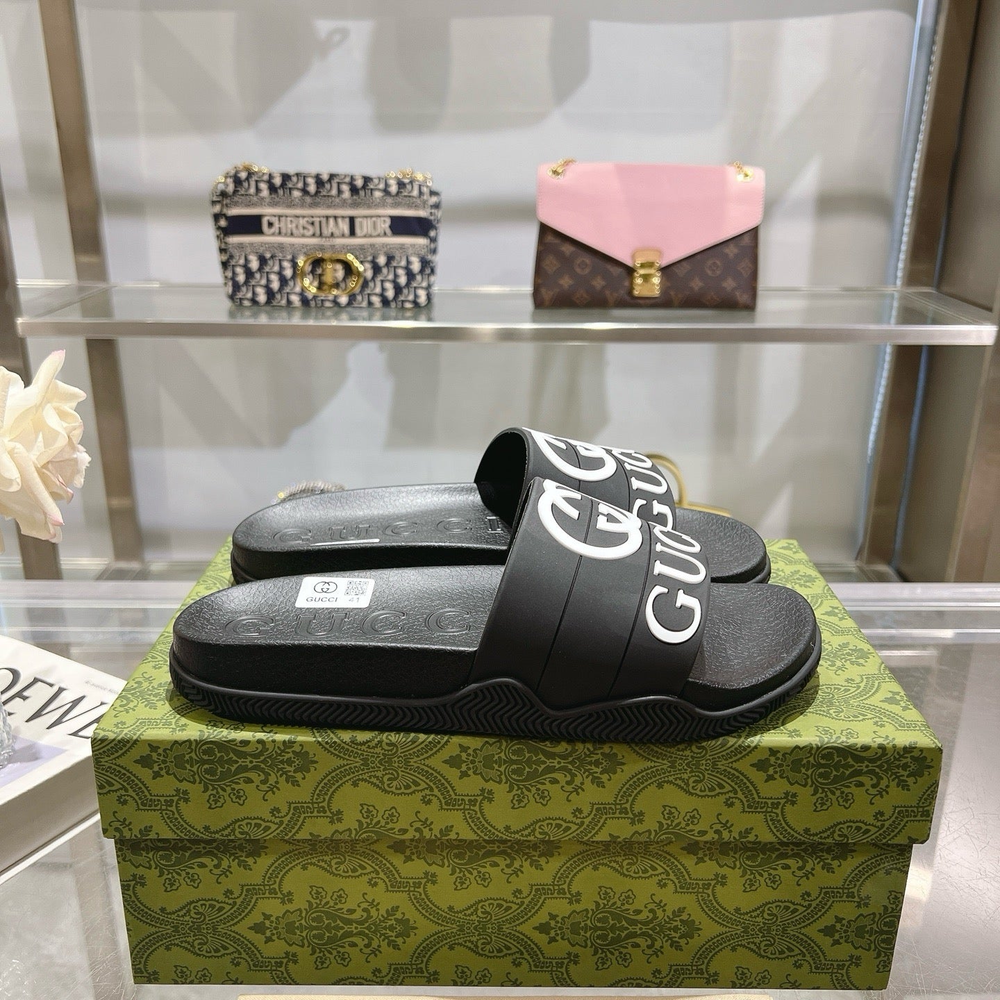 Black Gucci slide sandals on box, textured footbed with white logo strap