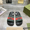 Black Gucci slide sandals with green strap, red stripe, and rubber footbed.