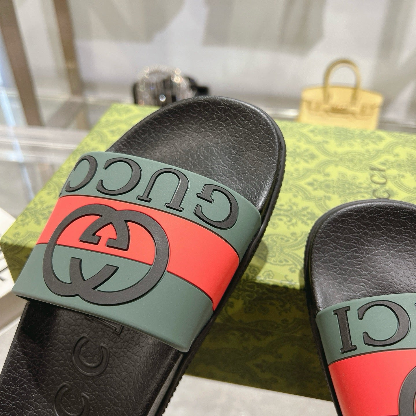 Black Gucci slide sandal with green strap, red stripe, and GG logo detail.